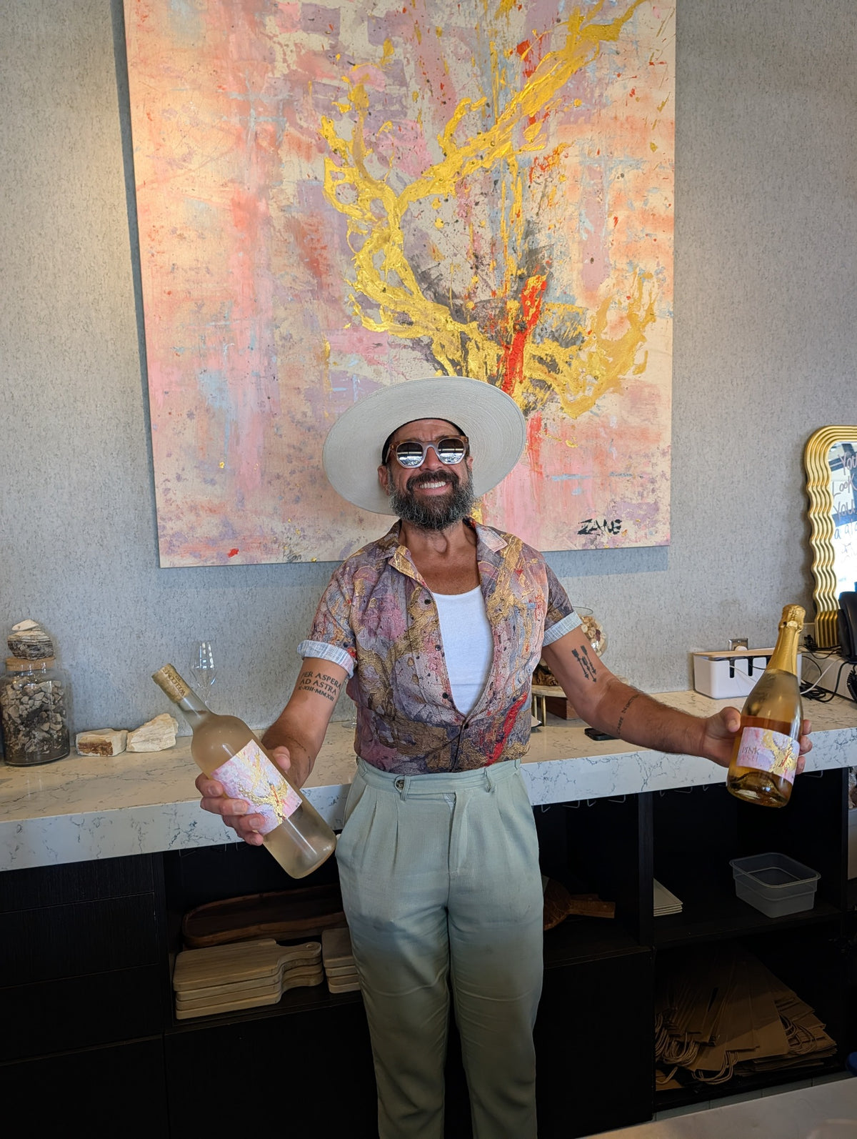 Person wearing the Pink Ash Paradise Yacht Rob Signature Shirt beside two wine bottles